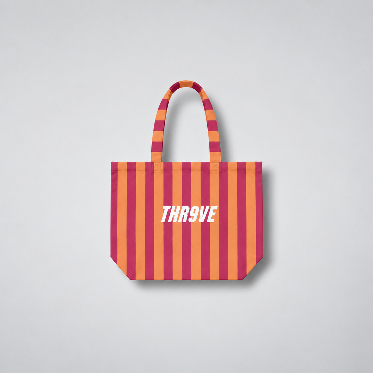A striped tote bag with alternating orange and magenta vertical stripes, featuring the word 'THR9VE' printed in white across the center. The bag has two top handles and is shown against a neutral light gray background.
